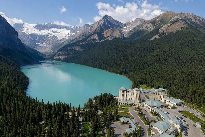 A mountain lake surrounded by forested mountains, a large hotel complex, and a clear sky. 5