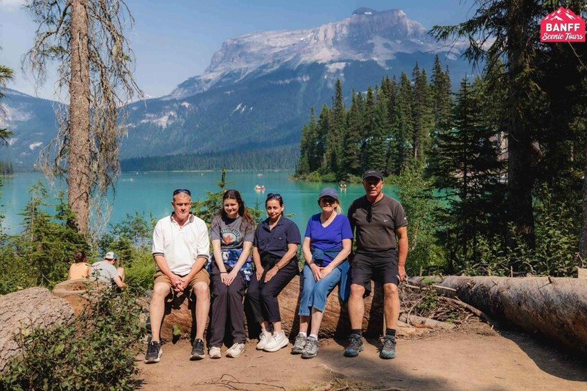 A group of people sitting on a dirt path with a mountainous landscape and a lake in the background. 2