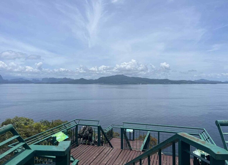 A wooden deck with railings overlooking a calm body of water and distant mountains under a partly cloudy sky. 4