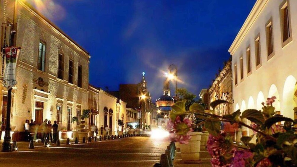 A nighttime street scene with illuminated buildings and a prominent dome structure in the distance. 1