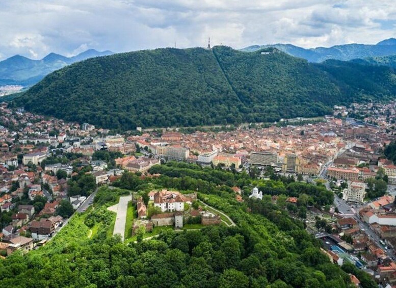 A city with a prominent hill, dense greenery, and a clear sky. 1
