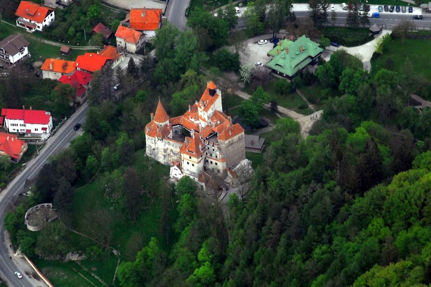 A castle with red roofs surrounded by greenery and a road nearby. 5