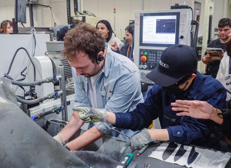 Two individuals working with machinery in an industrial setting, wearing gloves and safety equipment. 2