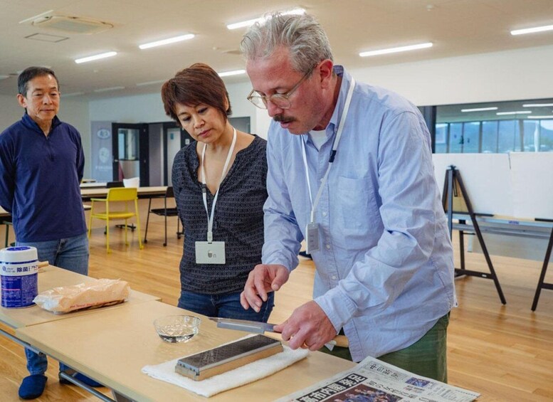 A person cutting a piece of material on a table in a room with chairs and a window. 5