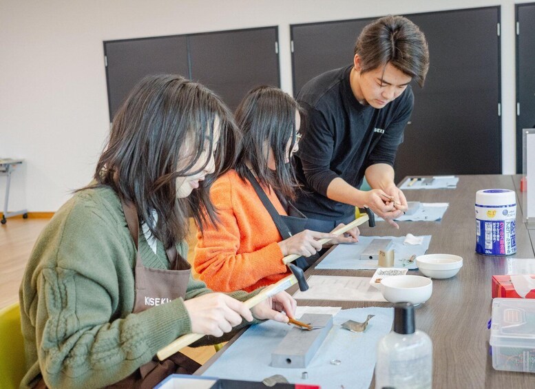 Three people engaged in a craft activity, possibly pottery or woodworking, with tools and materials on a table. 4