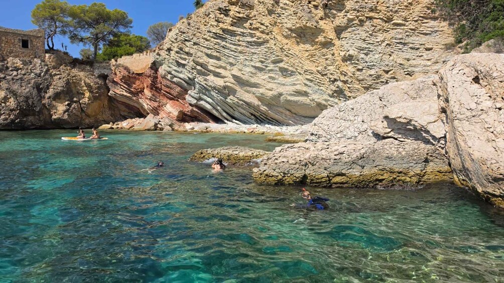 A coastal scene with clear turquoise water, rocky cliffs, and a small building. 4