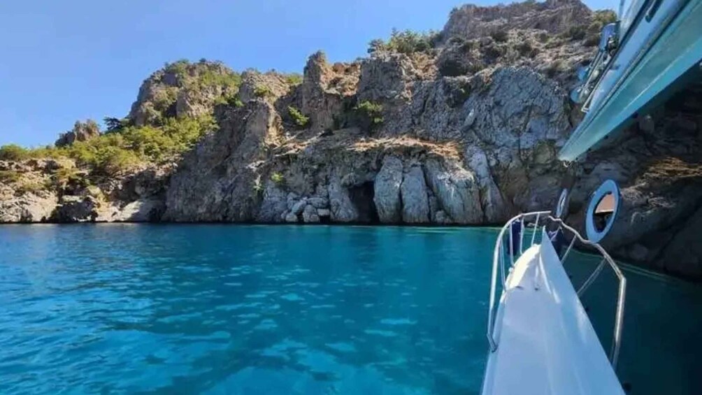 A boat on clear turquoise water with rocky cliffs and sparse vegetation in the background. 5
