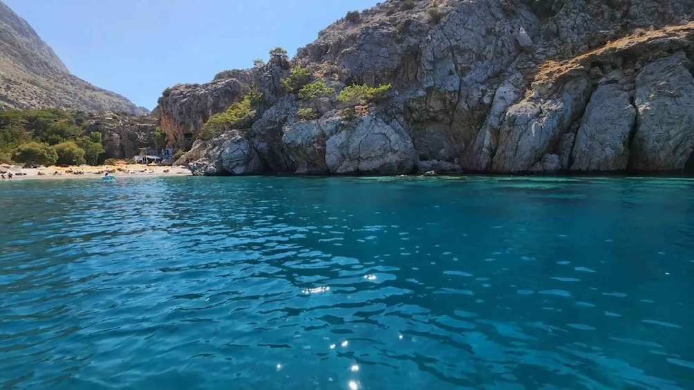 A coastal landscape with clear turquoise waters, rocky cliffs, and a beach. 1