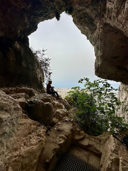 A person sitting on a rocky ledge, overlooking a cityscape through a natural archway. 5