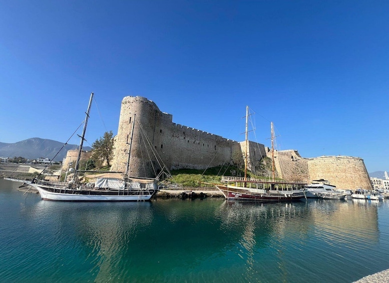 A historic castle by a calm harbor with sailing boats docked. 1