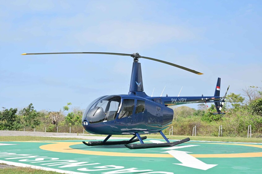 A blue helicopter with 'PX-VPY' on its tail rotor, parked on a green landing pad with white directional arrows. 5