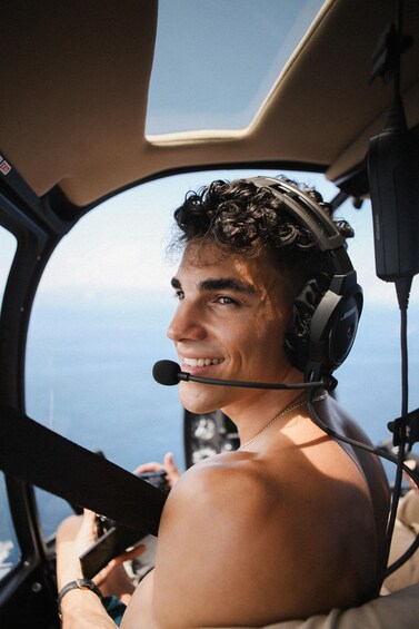 A person in a cockpit wearing a headset, with a view of the sky and clouds outside. 5