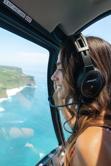 A person wearing headphones, looking out of an aircraft window at a coastline. 4