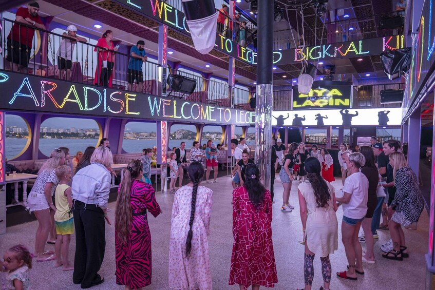 A crowded indoor venue with neon signs reading 'PARADISE' and 'WELCOME TO LEGEND.' 2
