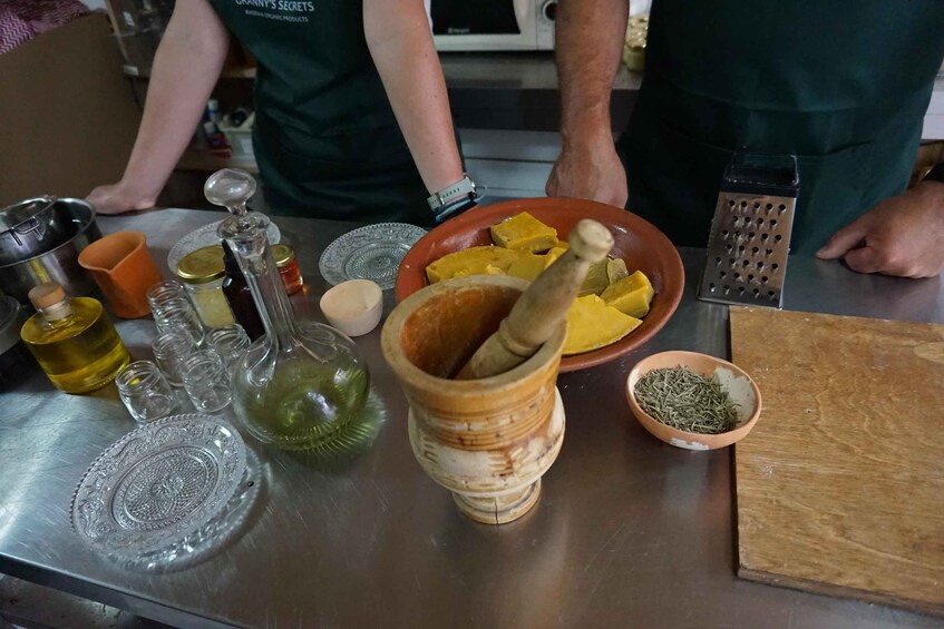 A kitchen counter with a mortar and pestle, a bowl of yellow squash, a grater, and various bottles and containers. 2