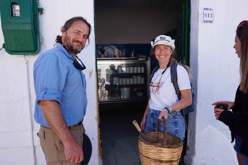 A man in a blue shirt and a woman in a white t-shirt with a white cap standing at a doorway, with a wicker basket in hand. 1