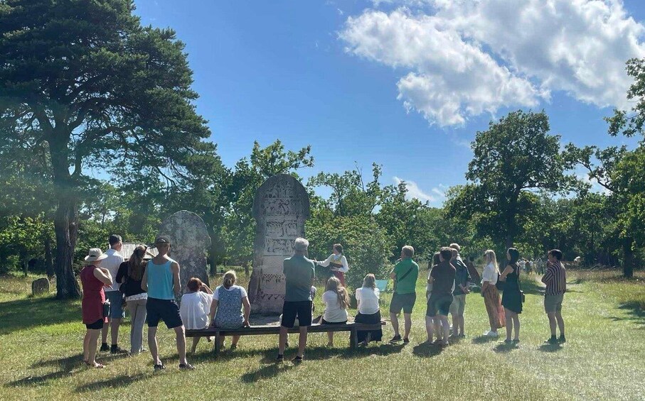 A group of people gathered around a large stone monument in a grassy park with trees in the background. 3