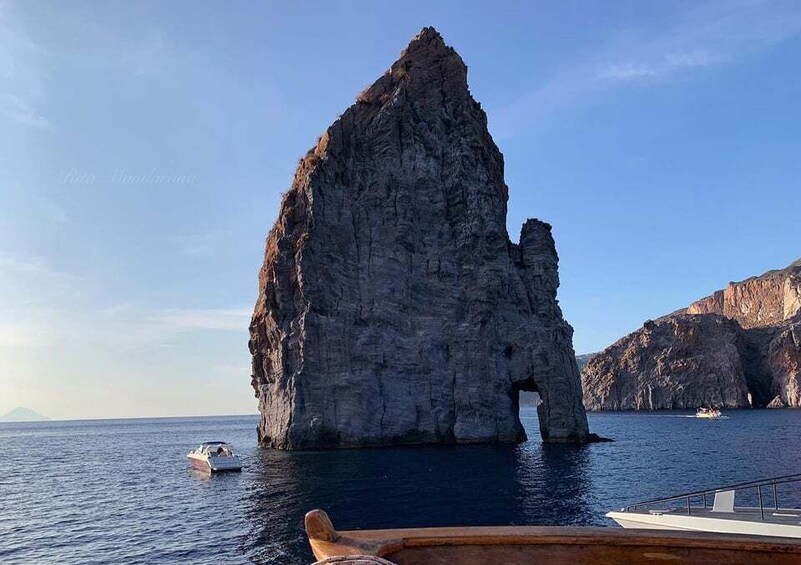 A large rock formation with a natural arch in the sea, surrounded by smaller rocks and a boat in the foreground. 3