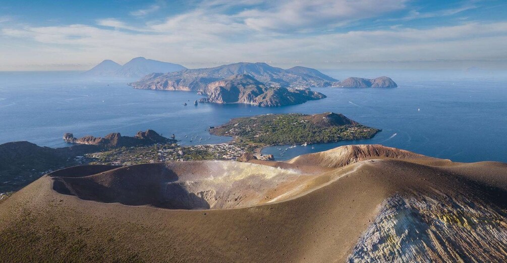 A coastal landscape with rugged terrain, a small island with vegetation, and a clear blue sea. 1