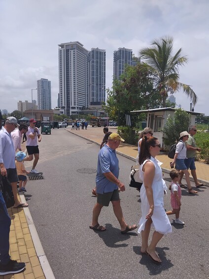 A group of people walking on a street lined with palm trees and tall buildings. 3