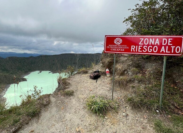A red sign indicating a high-risk area for civil protection, with a view of a turquoise lake and mountainous terrain. 2