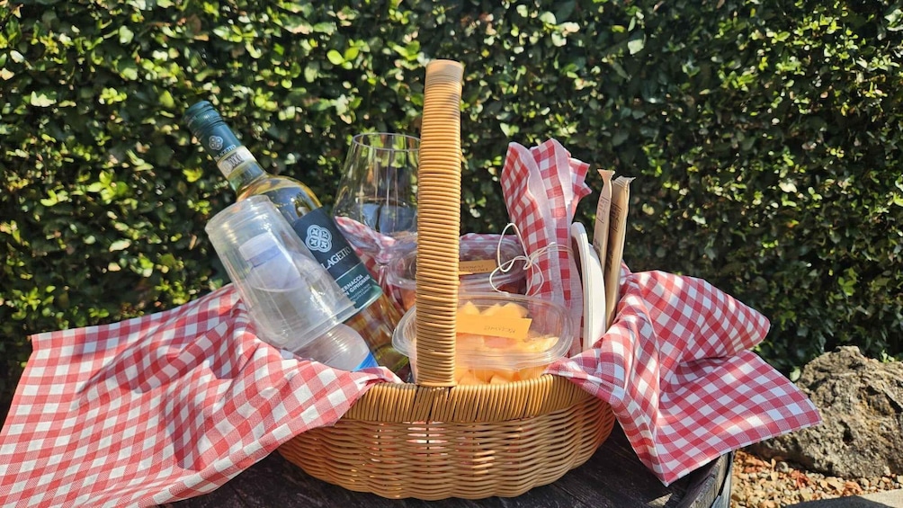 A picnic basket with a bottle, glasses, and a basket of food on a checkered cloth. 1