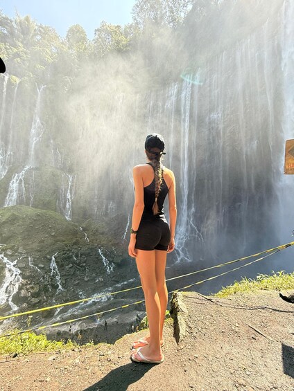 A person standing on a rocky ledge overlooking a waterfall. 5
