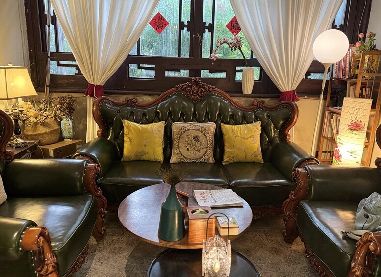 A traditional room with a green leather sofa, a round wooden coffee table, and a bookshelf with books and decorative items. 2