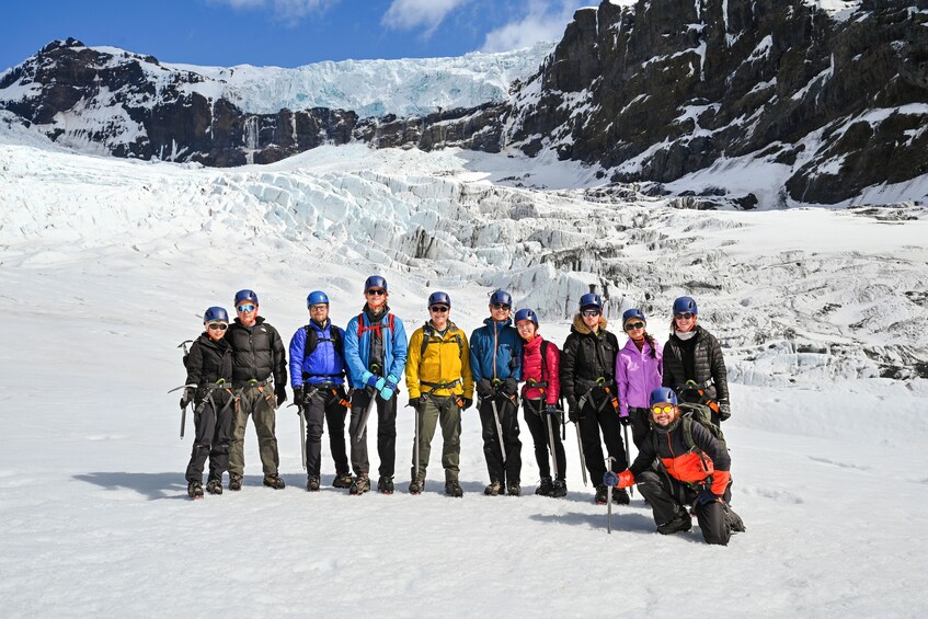 Un groupe de personnes, vêtues pour l’hiver, posent dans un paysage montagneux enneigé, avec un glacier en arrière-plan. 1