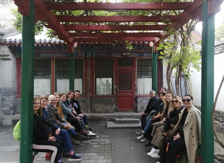 A group of people seated under a traditional Chinese pavilion with intricate designs and a red door. 1