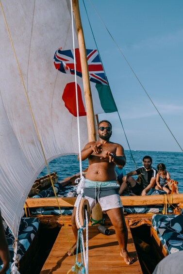 A person on a sailboat with a Union Jack flag, wooden deck, and ocean in the background. 3