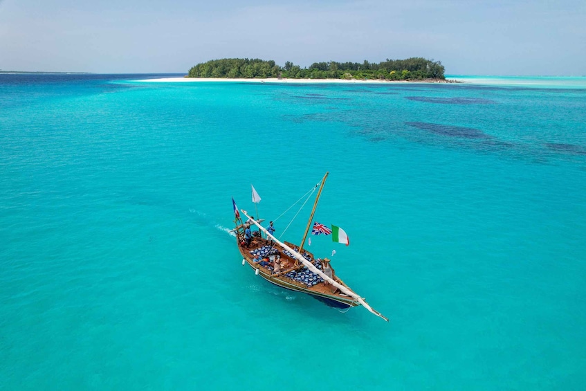 A boat with passengers and flags on turquoise waters with a small island in the background. 5
