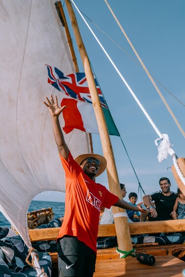 A person on a sailboat with a Union Jack flag, wearing a red shirt and a straw hat. 1