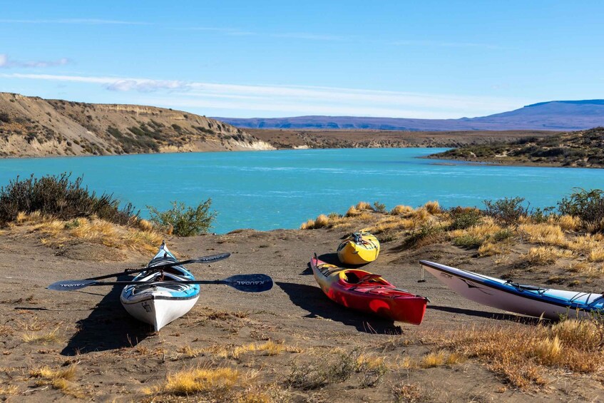 Three kayaks on a sandy beach with a lake and hills in the background. 1