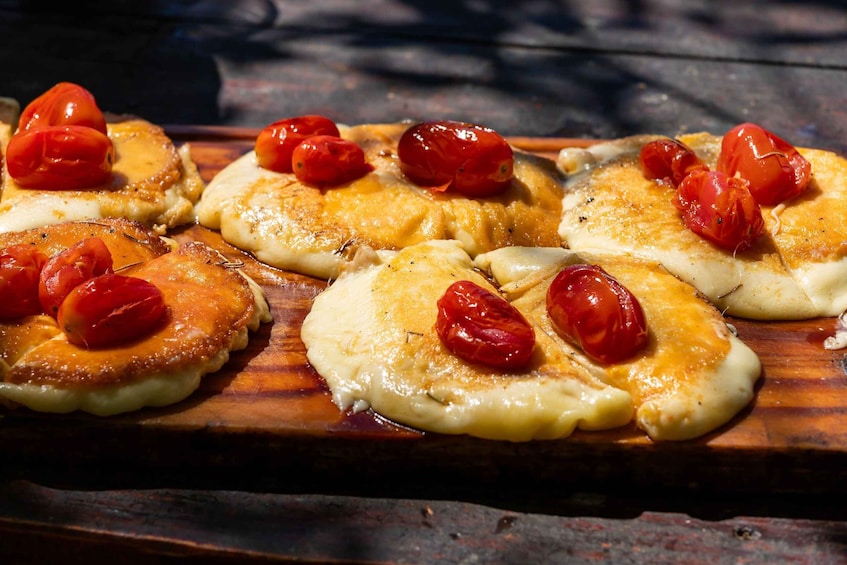 A wooden board with several pieces of food topped with red tomatoes. 3