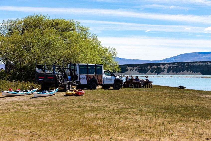 A safari vehicle, canoes, and people by a lake with mountains in the background. 5
