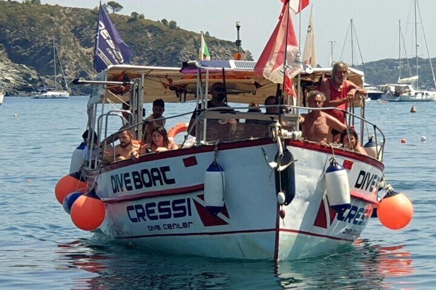 A white boat with 'DiveBoat' and 'Cressi' written on it, floating on water with people on board. 3