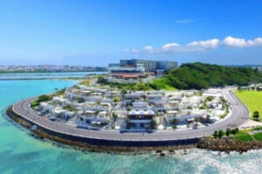A coastal development with a central building, a curved road, and surrounding greenery. 3