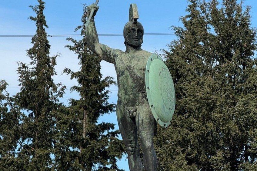 A statue of a warrior holding a shield and a spear, surrounded by trees. 1