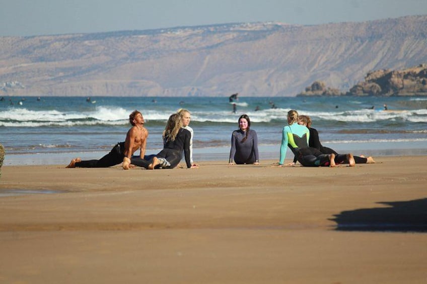 Un groupe de personnes pratiquant le yoga sur une plage, avec les vagues de l’océan en arrière-plan. 3