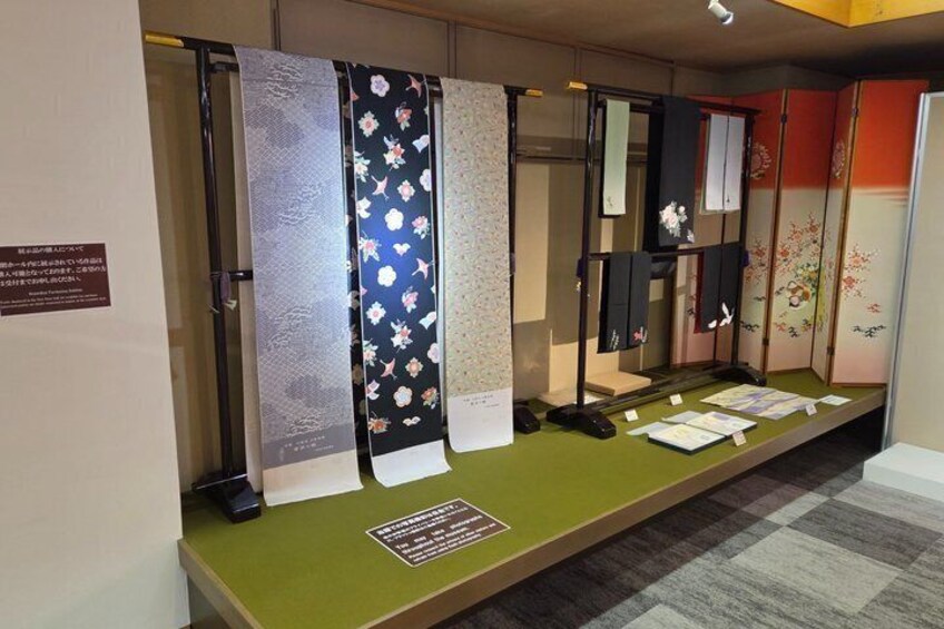 Une exposition de kimonos japonais traditionnels, présentés sur une table verte, accompagnée de panneaux explicatifs. 5