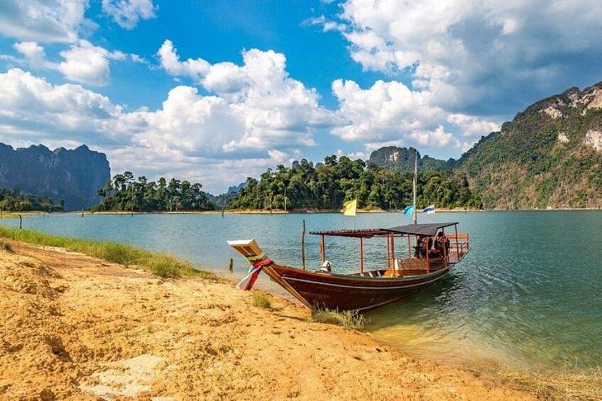 Ein Boot auf einem ruhigen See mit einem Sandufer, umgeben von Bergen und Bäumen. 5