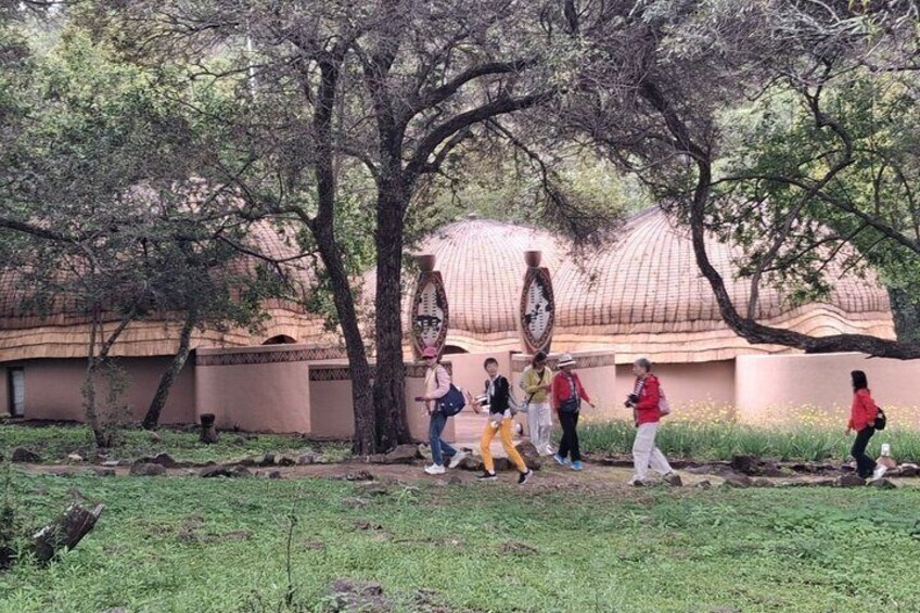 Un grupo de personas caminando por un parque con árboles y un edificio con un diseño arquitectónico llamativo al fondo. 3