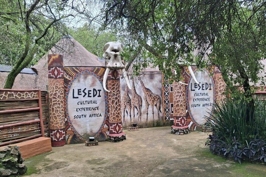 En port med giraffskulpturer och en skylt med texten ”Lesedi – en kulturell upplevelse i Sydafrika”. 1