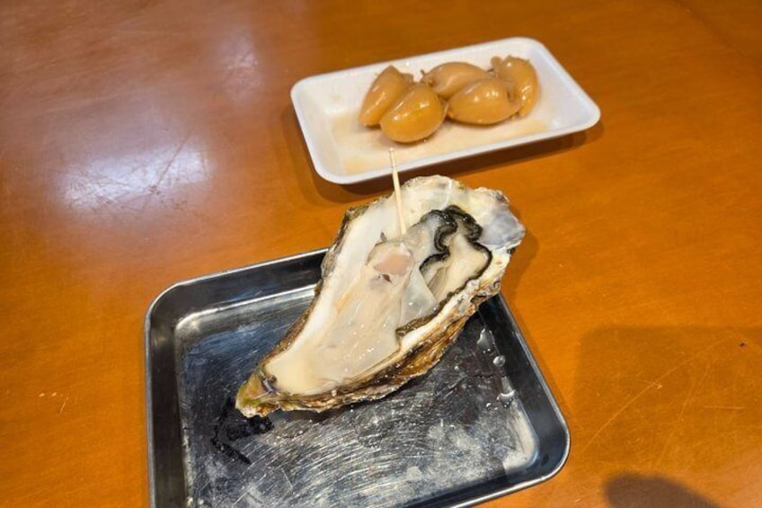 A half shell oyster on a black tray with a toothpick, and a plate of preserved lemons in the background. 4
