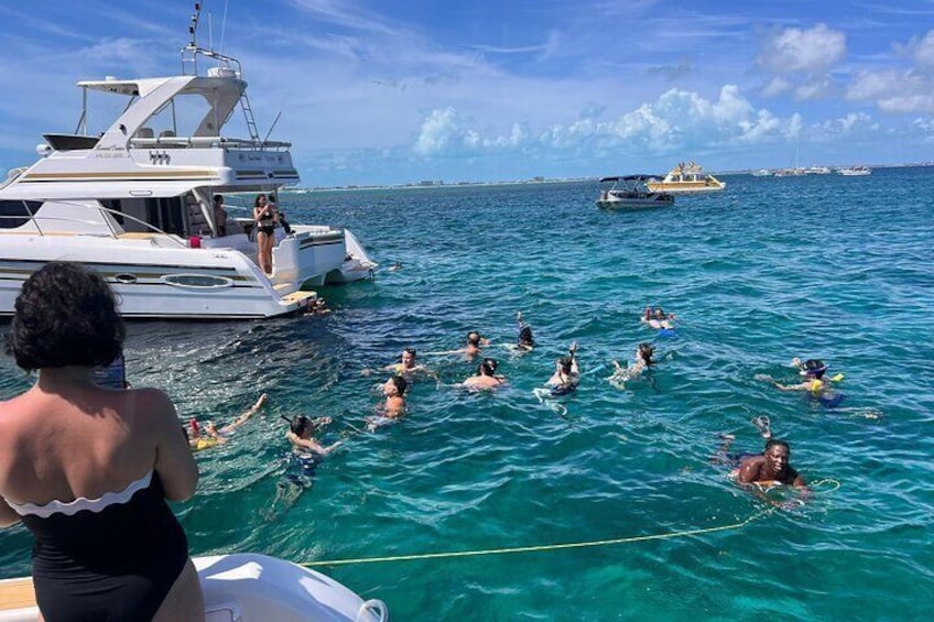 Un gruppo di persone che nuota e galleggia nell'oceano, uno yacht e altre imbarcazioni sullo sfondo. 2