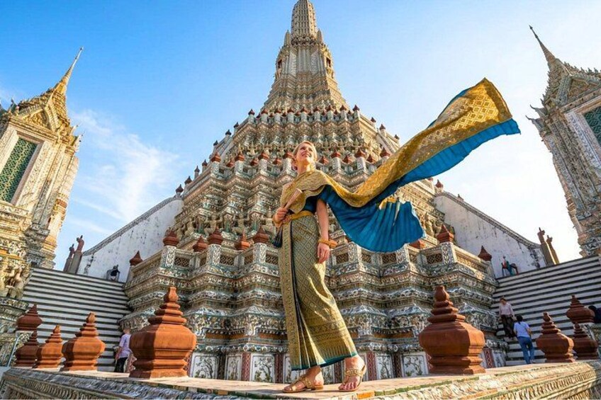 A person in traditional attire standing in front of a temple with intricate architecture. 1