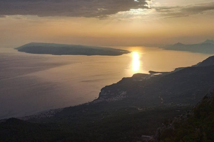 A coastal landscape with a sunset over the water, cliffs, and distant landforms. 4