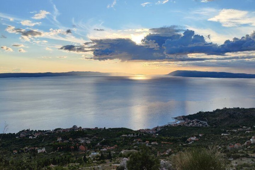 A coastal landscape with a sunset over the water, a distant mountain range, and a small settlement with houses. 5