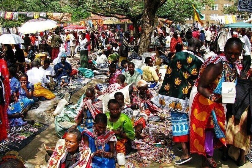 Un mercato all'aperto affollato, con persone sedute e in piedi, circondate da numerosi articoli e bancarelle. 1